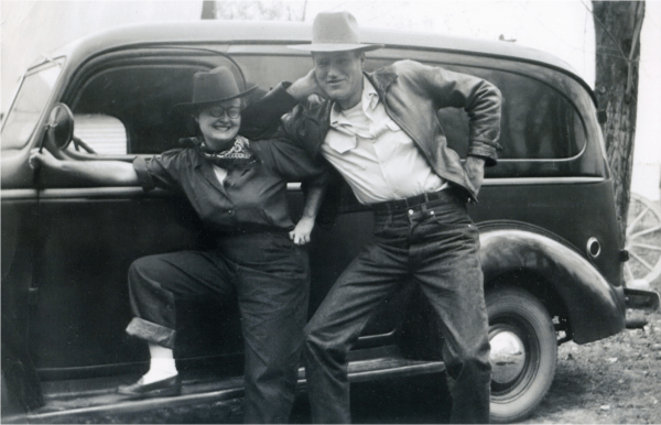Eileen Blakely and her husband posing in jeans and fedoras in front of a 1950s era car. 